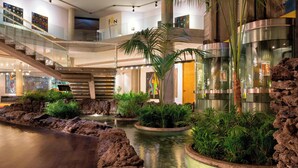 A modern indoor atrium with a central water feature, surrounded by planters and a glass railing. - Four Points by Sheraton Catania Hotel & Conference Center (Aci Castello)