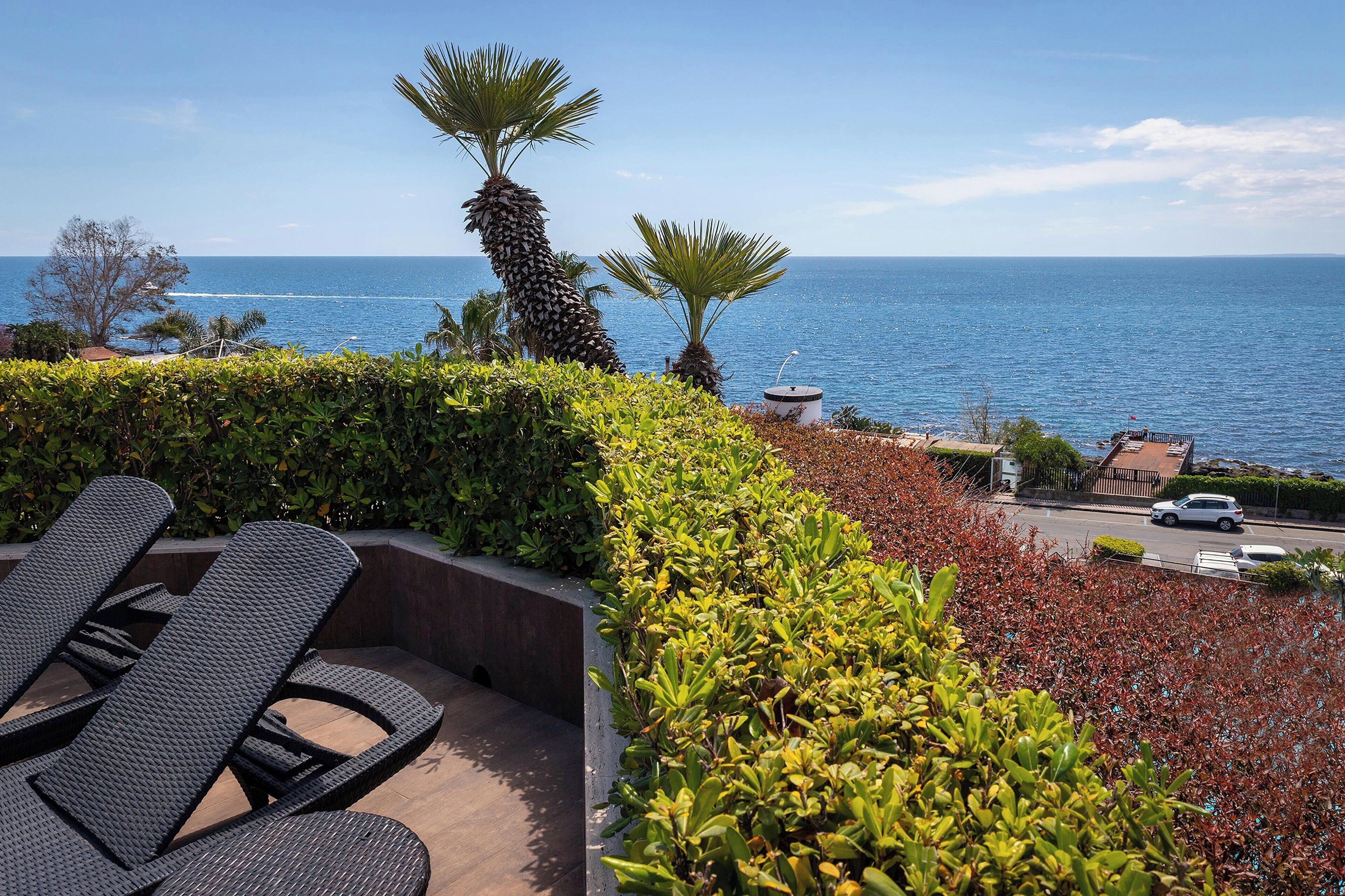 Une terrasse avec des chaises longues, une vue sur la mer et un espace de stationnement.