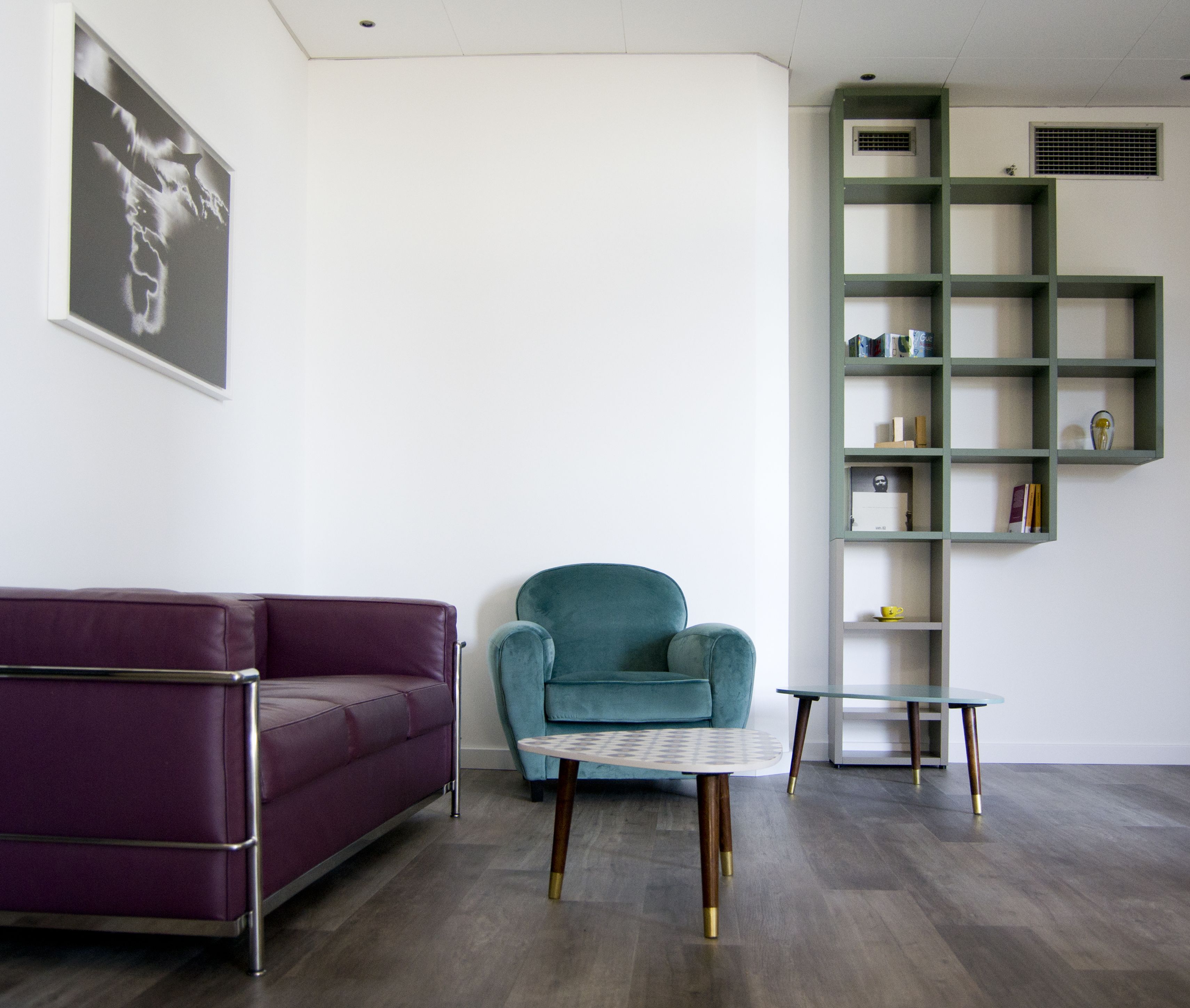 Una sala moderna con un sofá morado, un sillón turquesa y una mesa de centro de vidrio.
