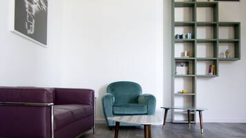 Una sala moderna con un sofá morado, un sillón turquesa y una mesa de centro de vidrio.
