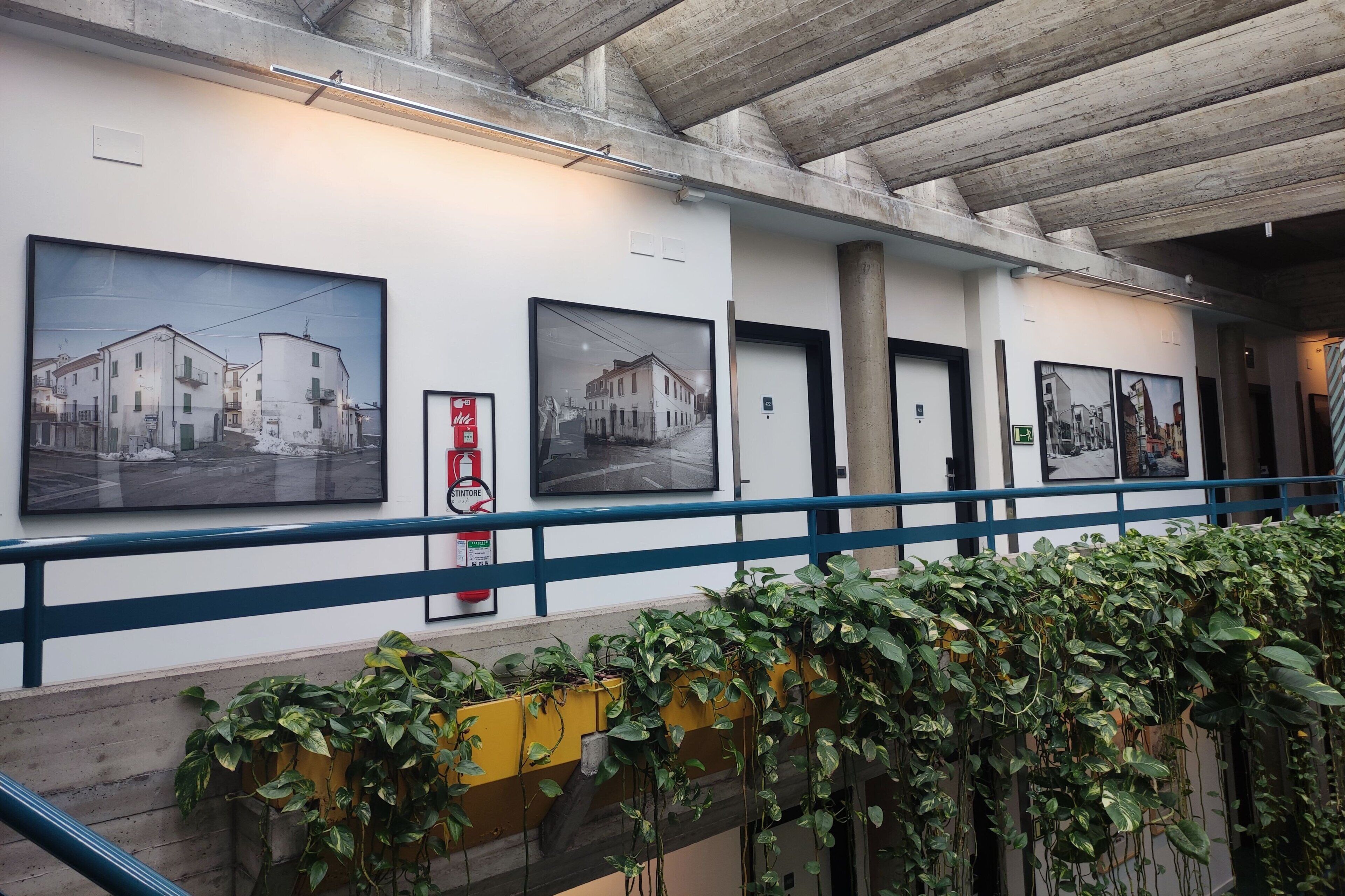 A hallway with framed black and white photographs on the walls, a fire extinguisher, and a blue railing.