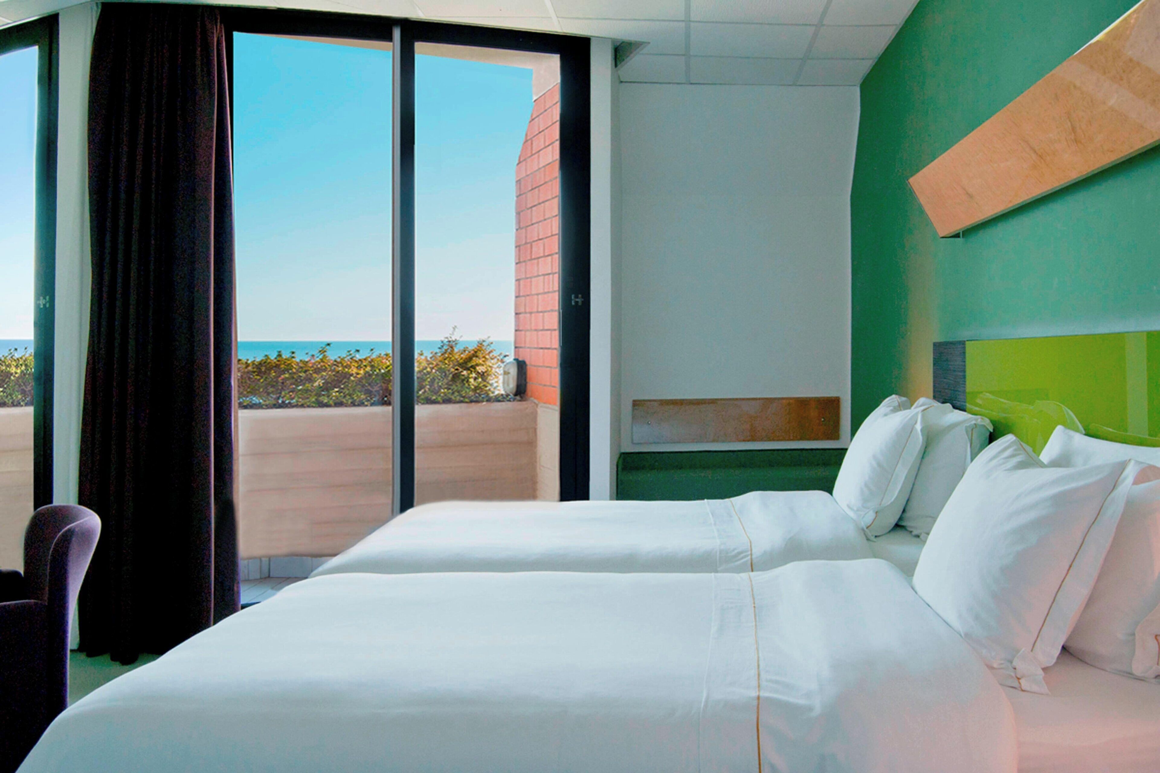 Ein Hotelzimmer mit zwei Betten, Meerblick und einer grünen Akzentwand.