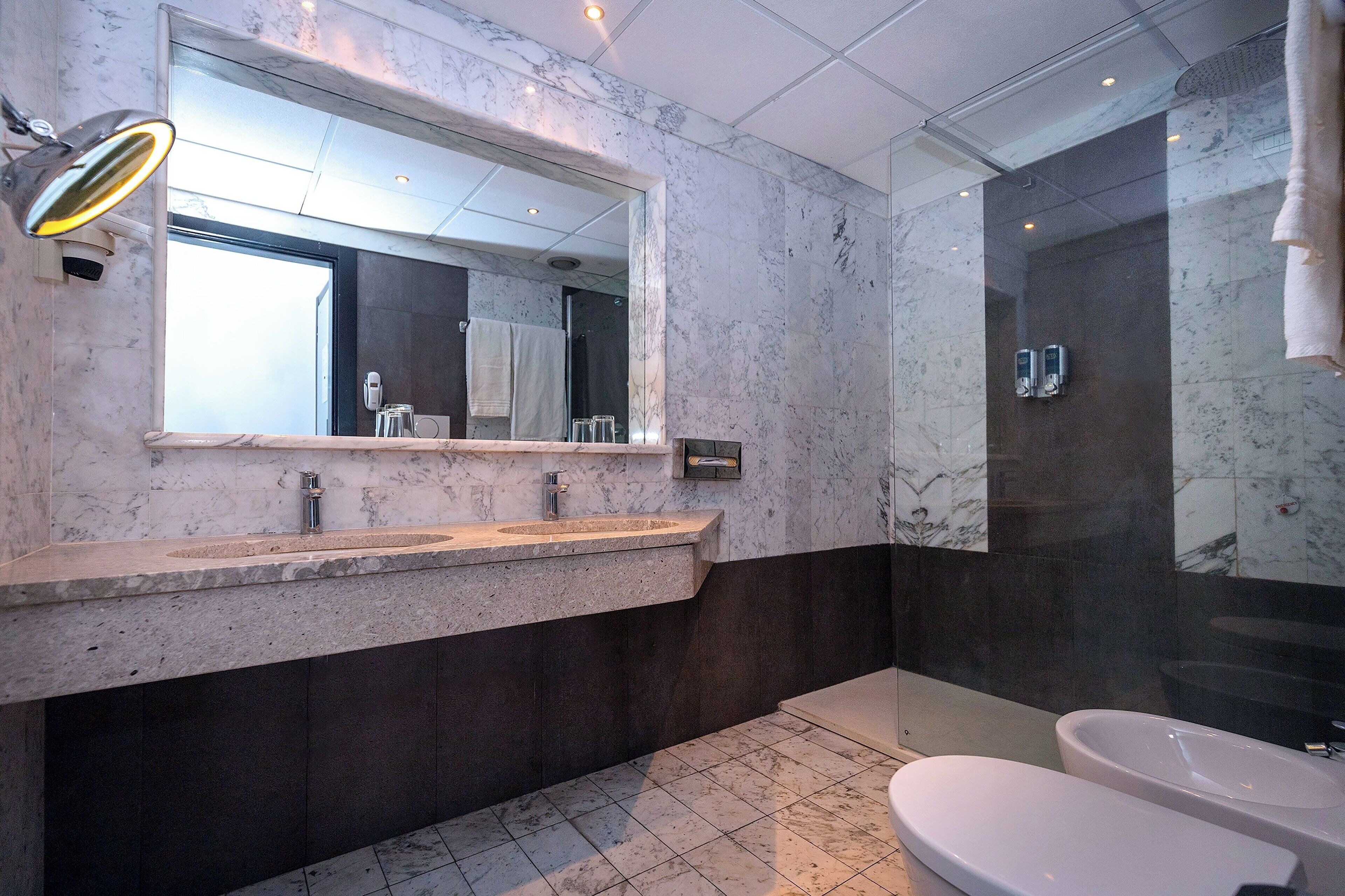 A modern bathroom with a marble vanity, a large mirror, a glass-enclosed shower, and a separate bathtub.