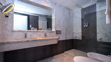 Un baño moderno con tocador de mármol, un espejo grande, ducha con cerramiento de vidrio y bañera separada.