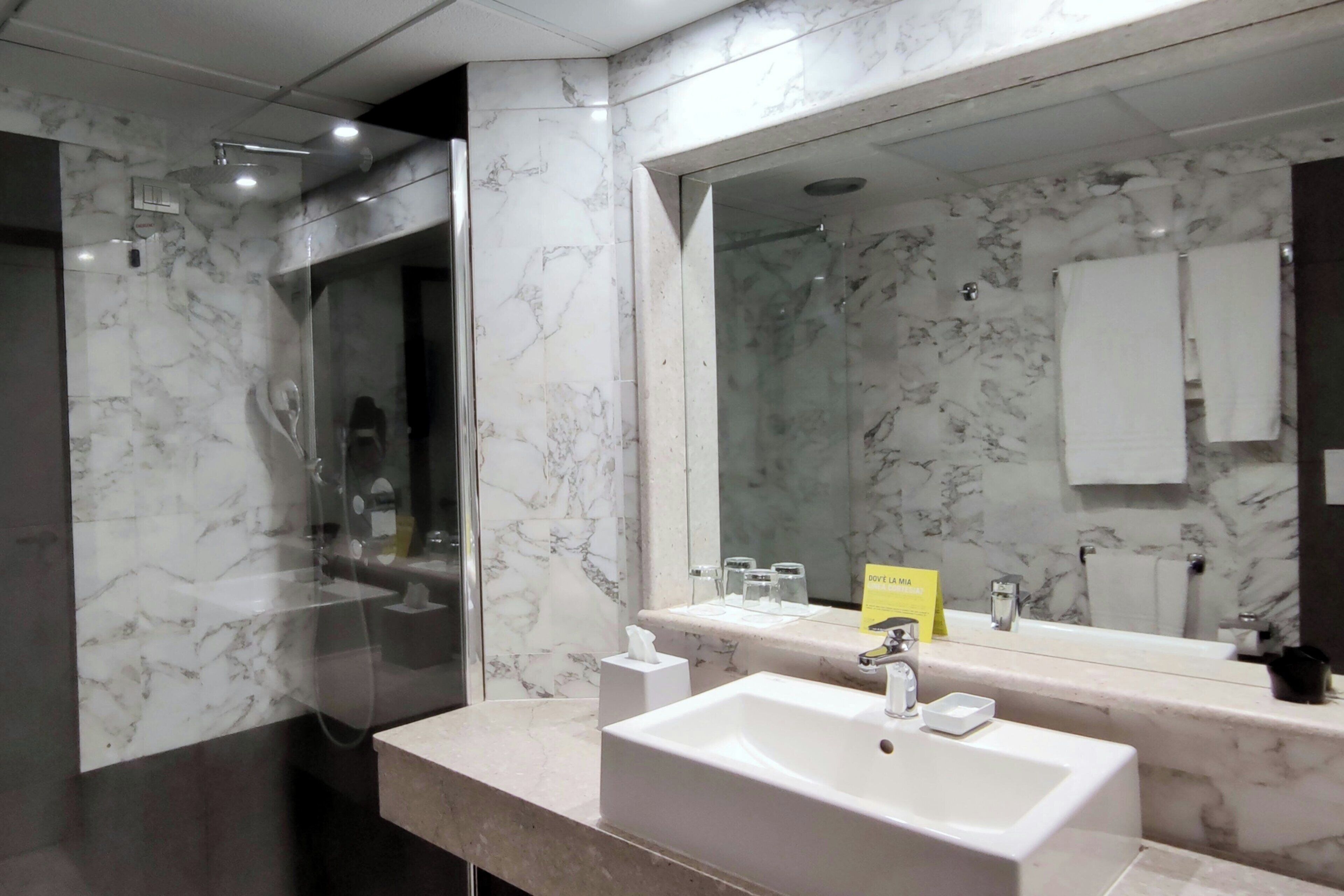 A modern bathroom with a marble vanity, a large mirror, and a glass-enclosed shower.