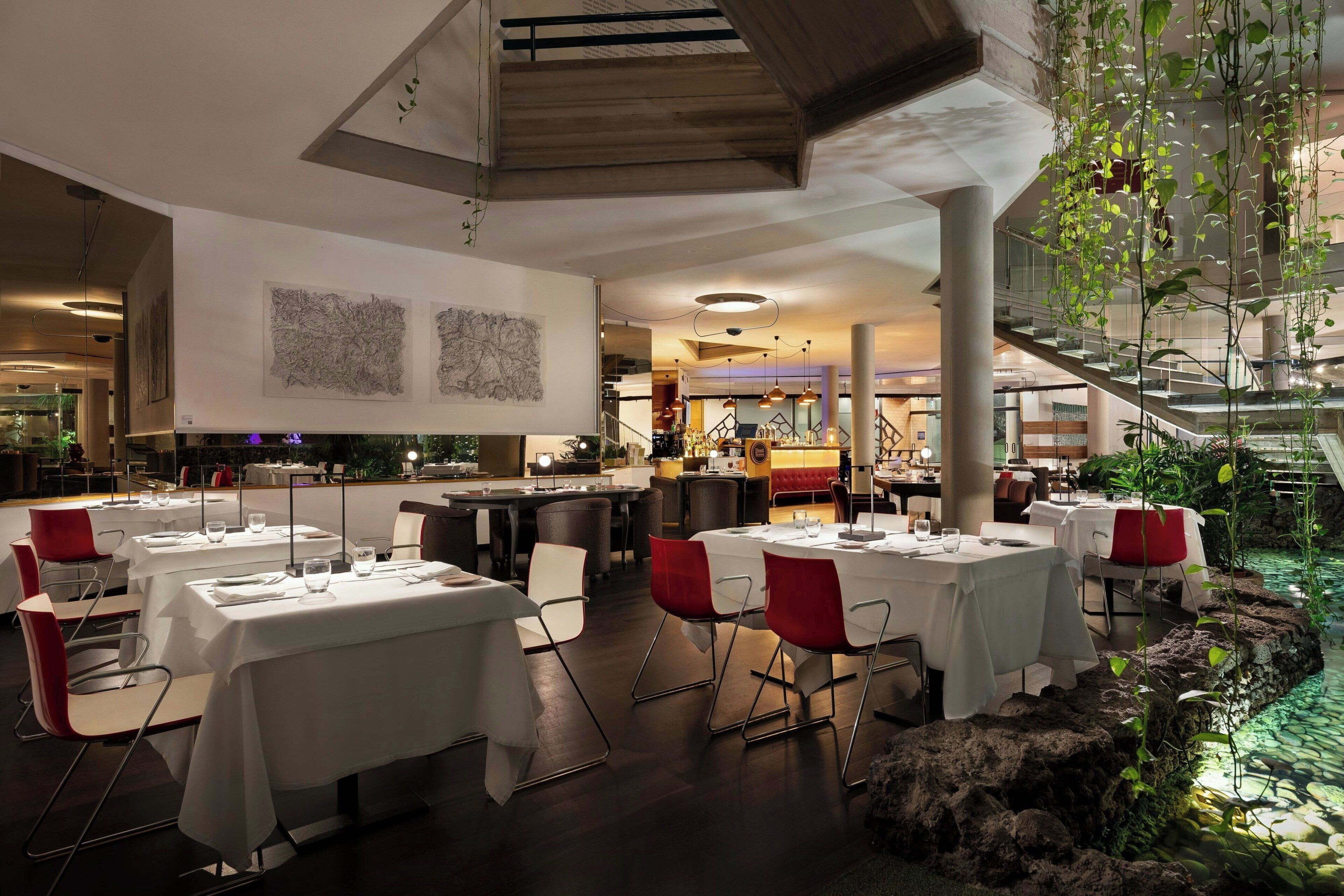 Un restaurante moderno con manteles blancos, sillas rojas y una escalera central.