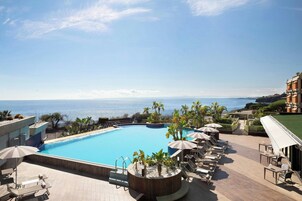 Una piscina en la azotea con vistas al mar, rodeada de sillones de playa y sombrillas.