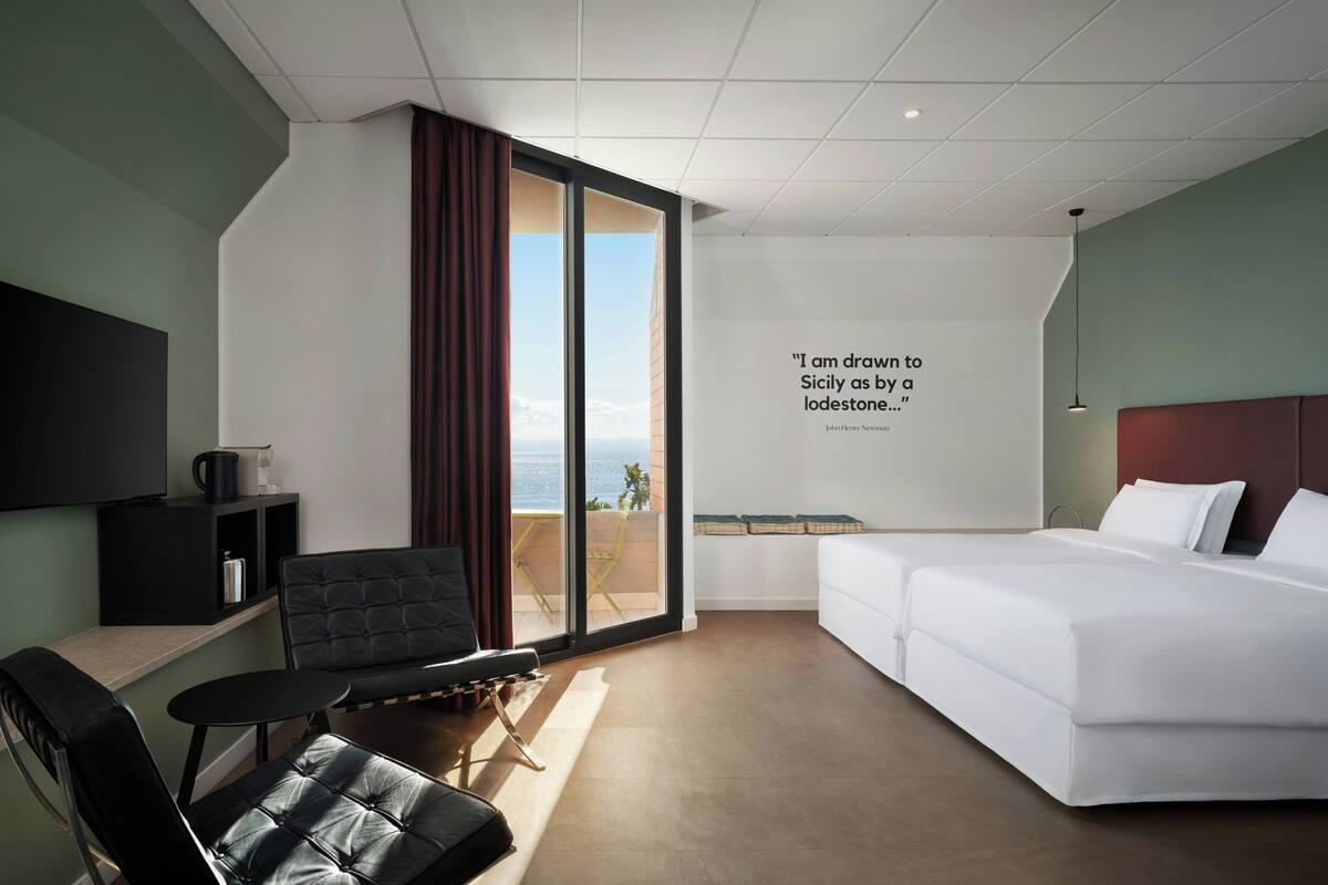 Een moderne hotelkamer met een groot bed, een bank, een stoel, een klein tafeltje en uitzicht op zee.