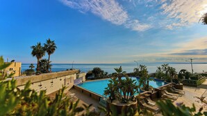 A rooftop pool with palm trees, a view of the sea, and a clear sky. - Four Points by Sheraton Catania Hotel & Conference Center (Aci Castello)