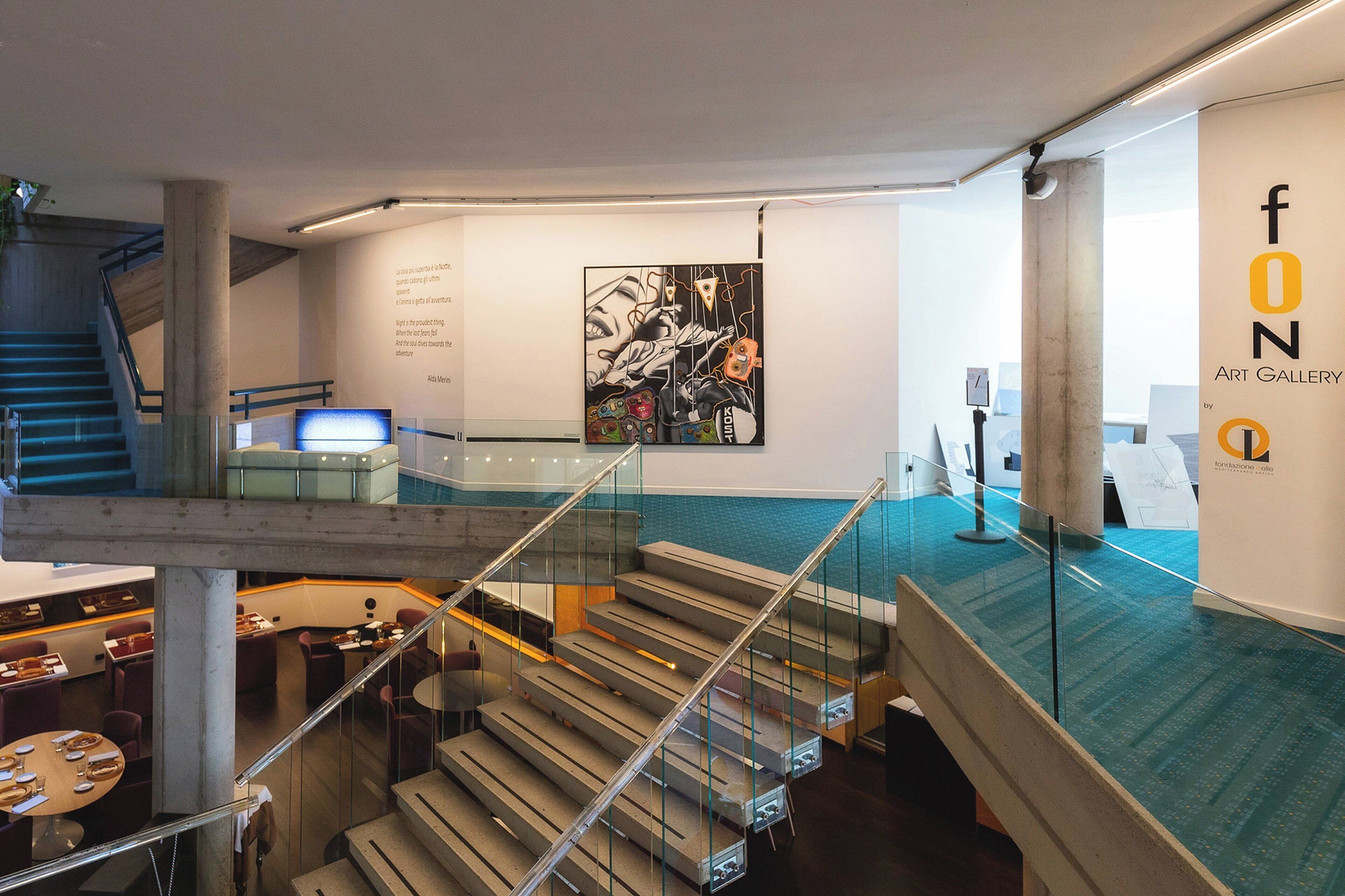 Une galerie d’art contemporain dotée d’un escalier reliant deux étages, avec des rampes en verre et un design minimaliste.