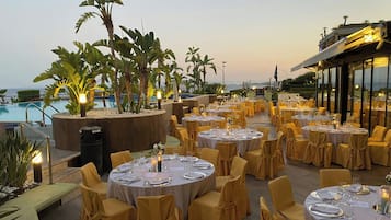 An outdoor dining area with round tables set for a formal event, surrounded by yellow chairs and plants.