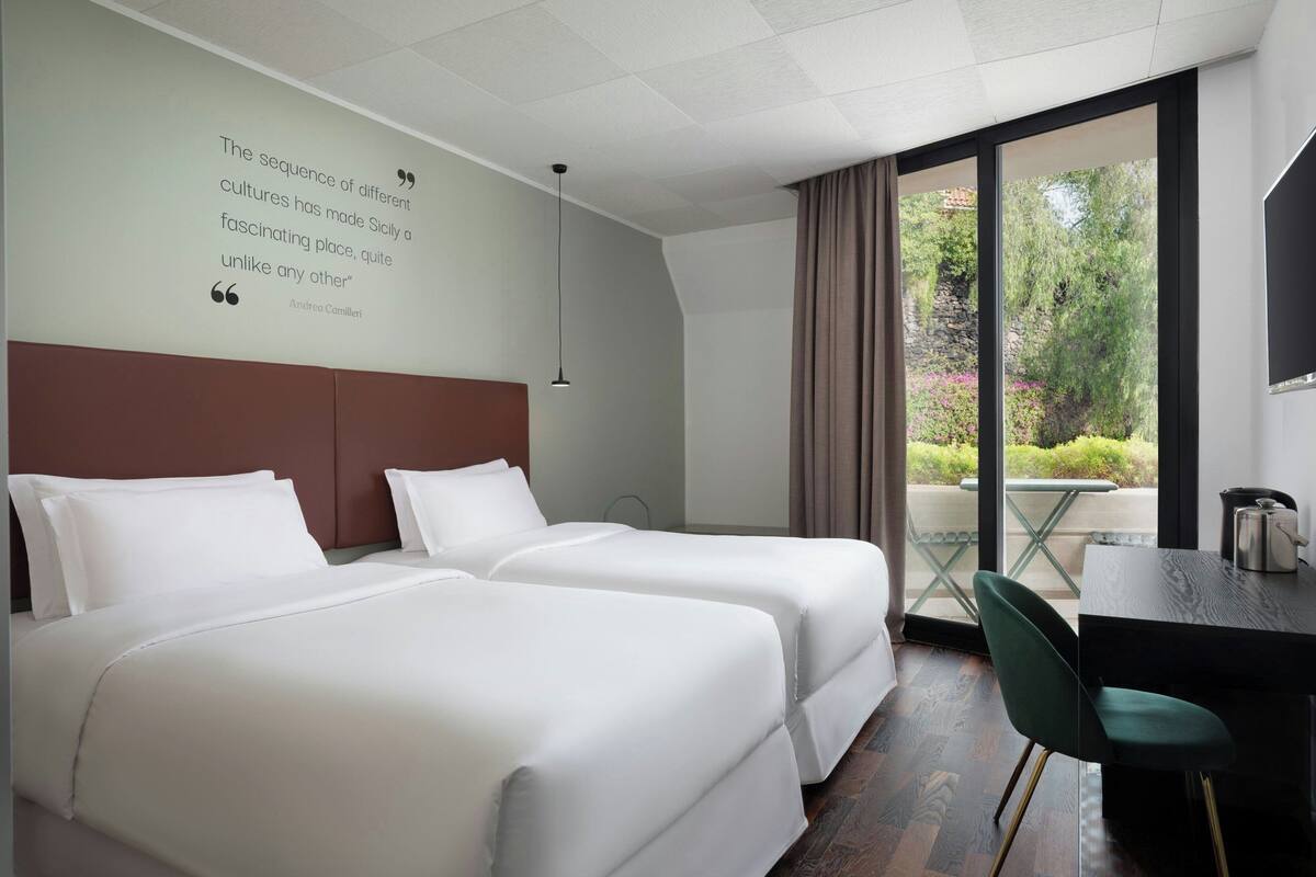 Een hotelkamer met twee bedden, een bureau en uitzicht op de omgeving.
