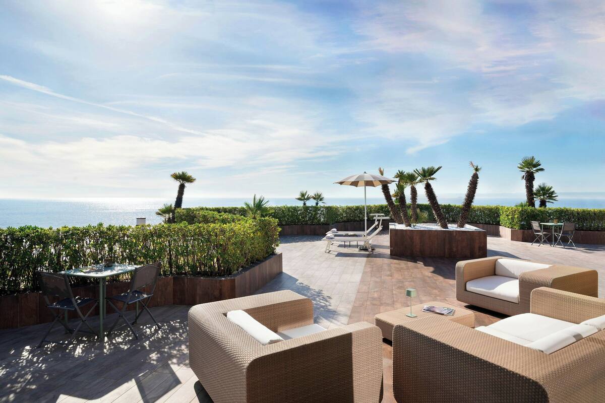 Een terras met rieten meubilair, een tafel en stoelen met uitzicht op een waterpartij.