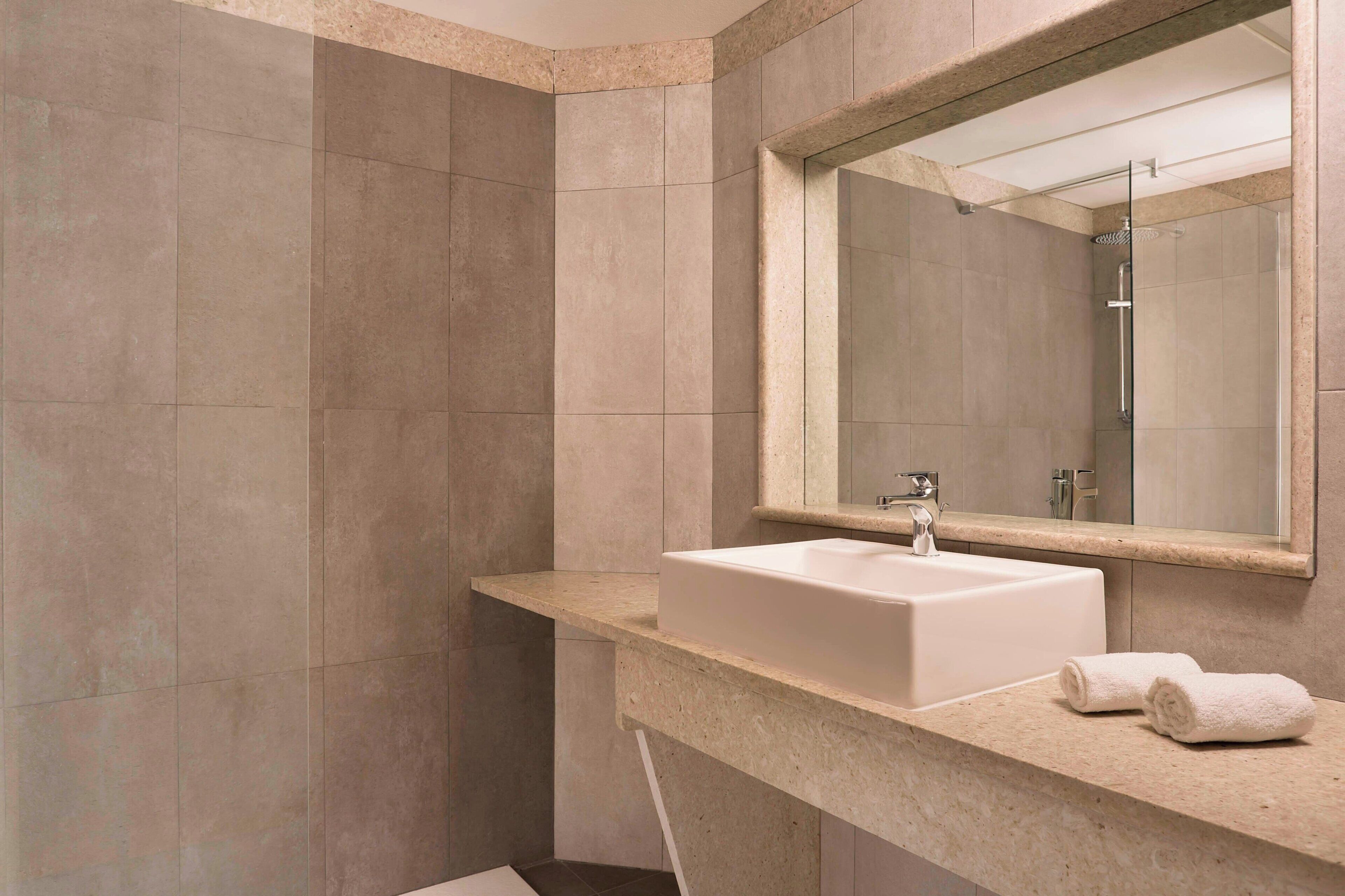 A modern bathroom with a large mirror, a sink, and a shower.