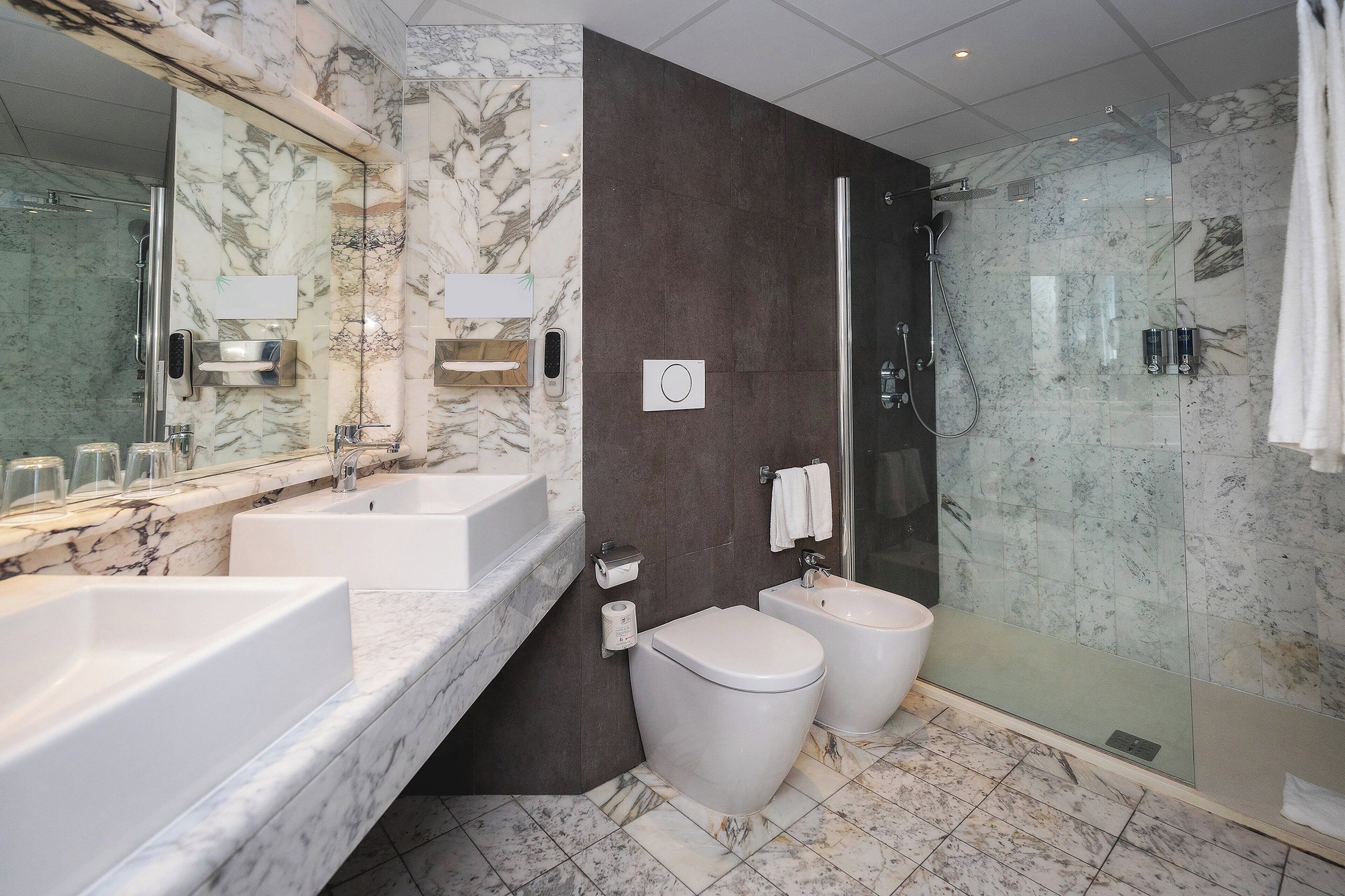 Une salle de bain moderne avec des comptoirs en marbre, une douche à parois de verre et des toilettes.