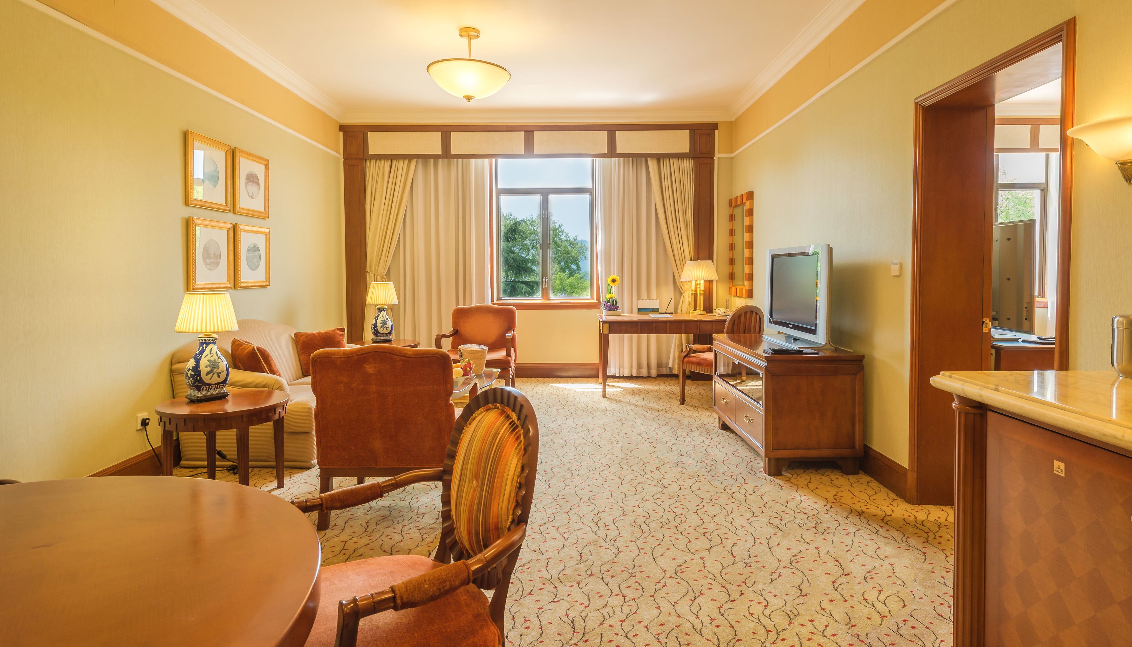 Une chambre d’hôtel équipée d’un canapé, de fauteuils, d’une table à manger, d’un téléviseur et d’un bureau avec une lampe.