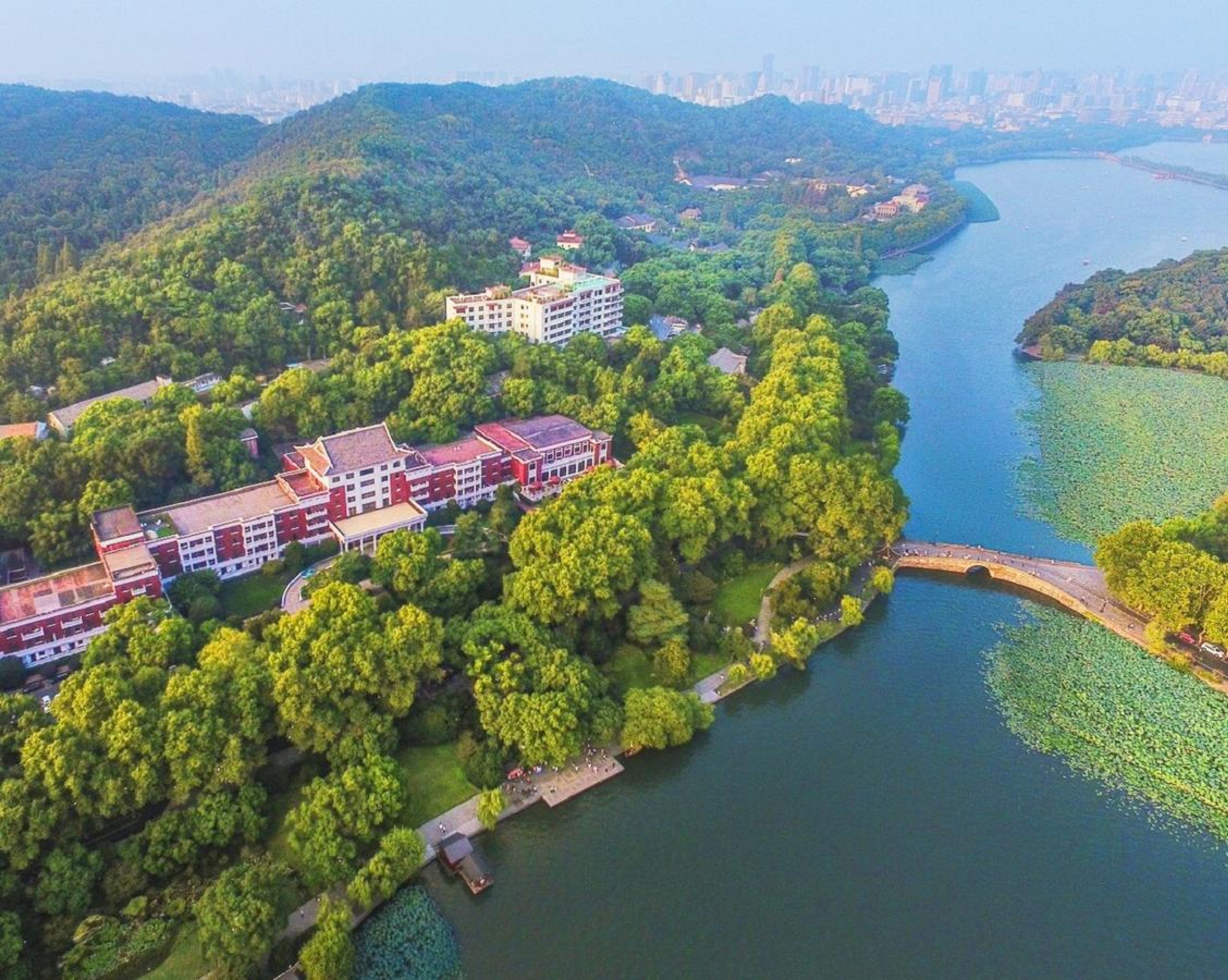 An aerial view of a campus with buildings surrounded by lush greenery and a river.