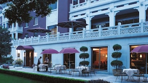 Hotel com área de estar ao ar livre, coberta por guarda-sóis, e um jardim bem cuidado.