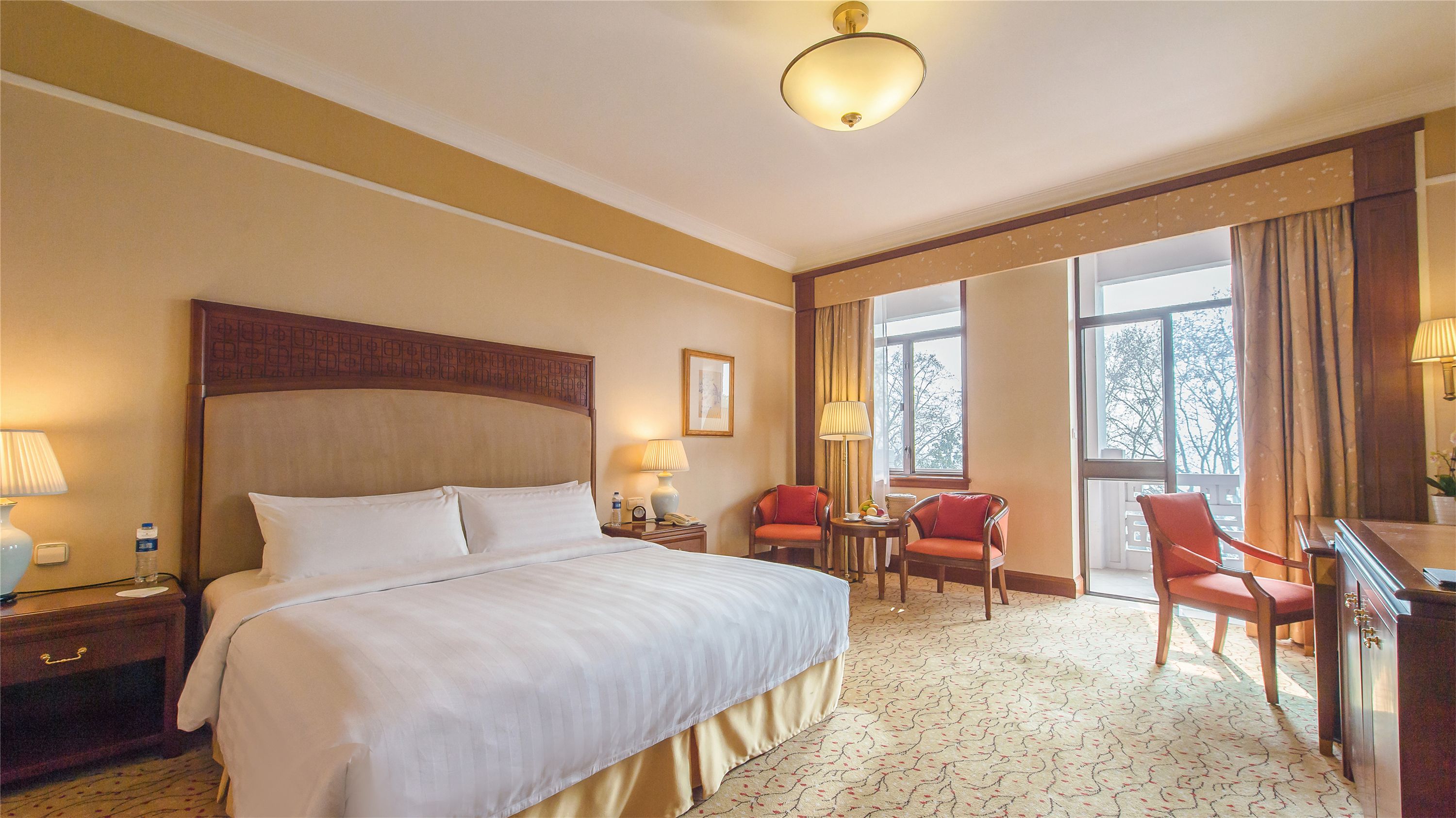 A hotel room with a large bed, two chairs, a desk, and a window with curtains.