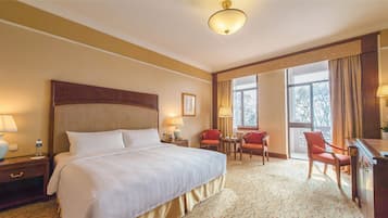 A hotel room with a large bed, two chairs, a desk, and a window with curtains.