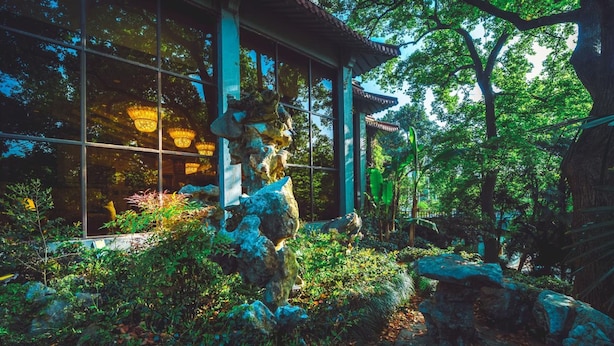 Um edifício japonês tradicional com um jardim de pedras, rodeado por vegetação exuberante e árvores.