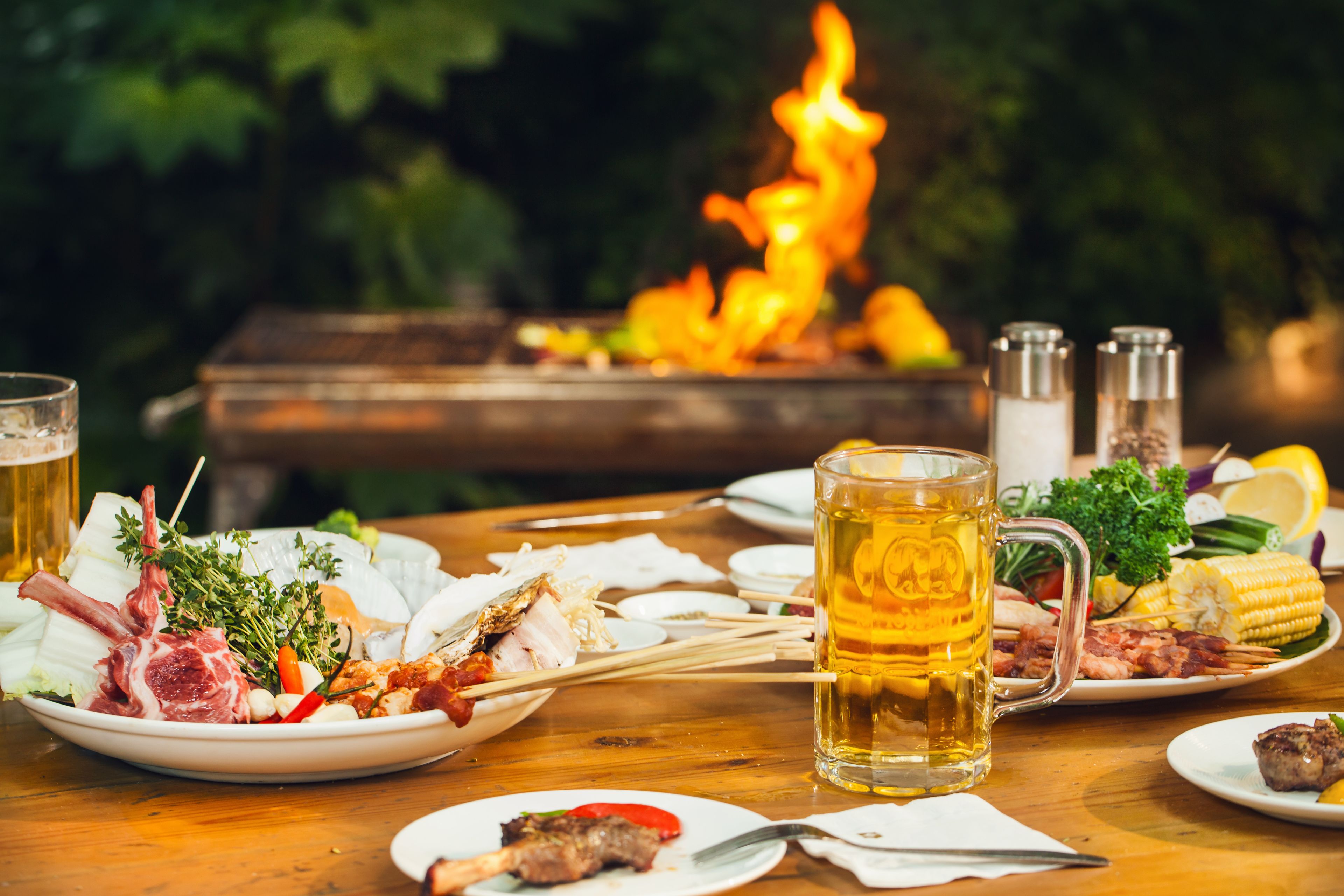 A dining table with various dishes, a beer mug, and a fire pit in the background.