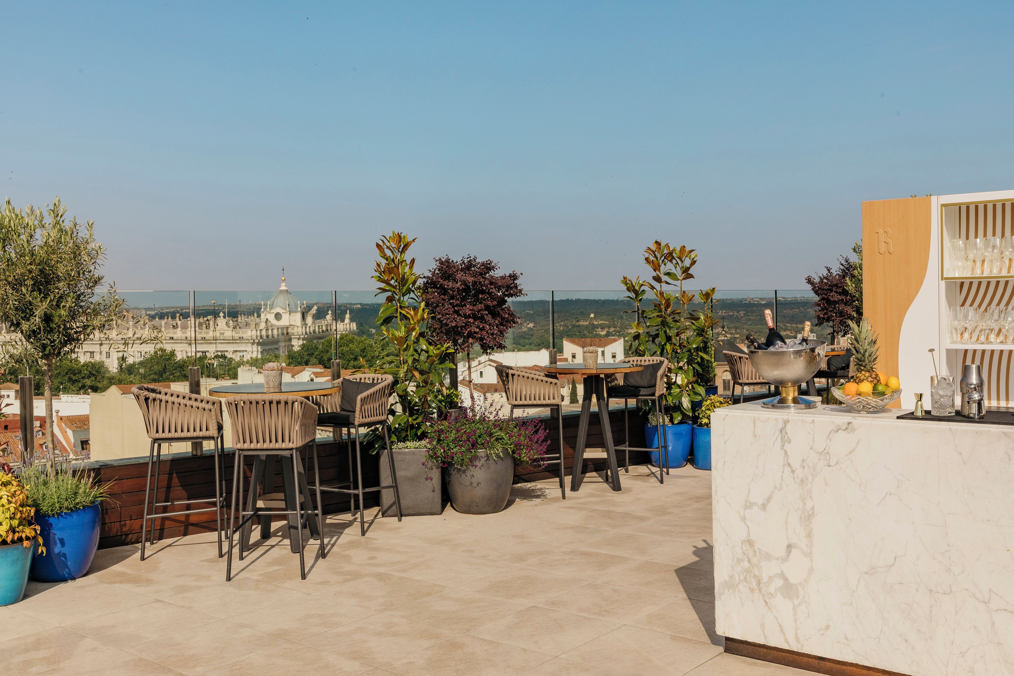 A rooftop terrace with outdoor seating, potted plants, and a view of the cityscape.