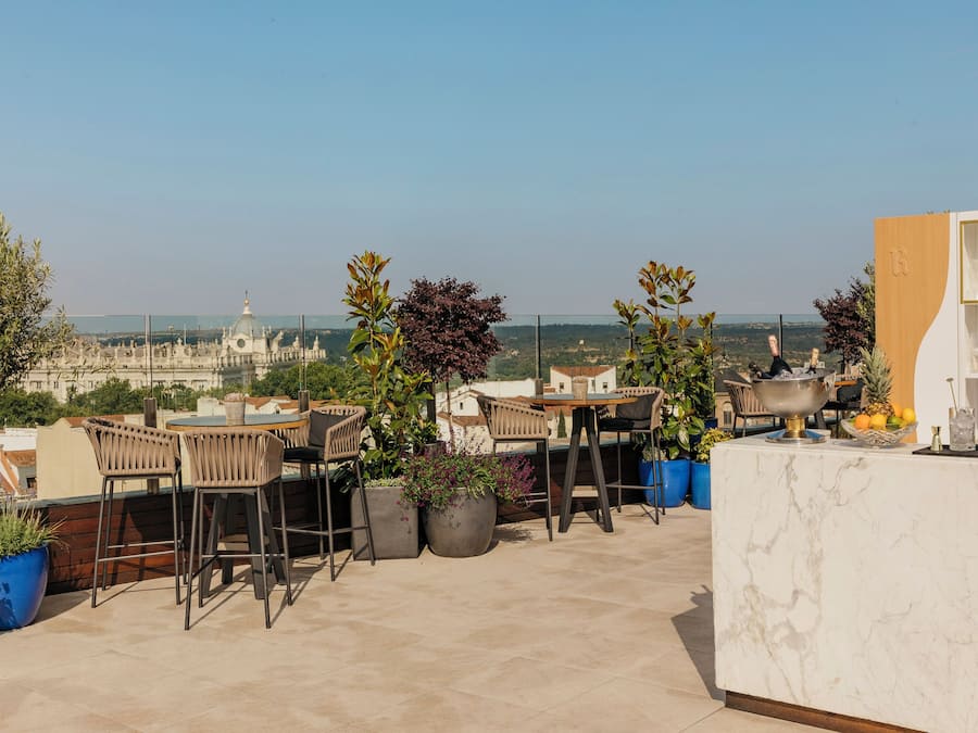 Eine Dachterrasse mit Sitzgelegenheiten im Freien, Blumentöpfen und Blick auf die Stadtlandschaft.