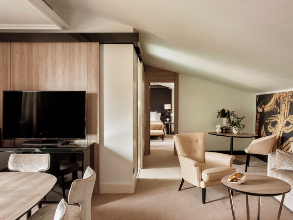 A modern hotel room with a flat-screen TV, a dining area with a table and chairs, a sofa, and a small side table with a bowl.