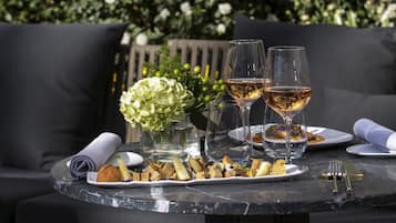 Una mesa de comedor al aire libre con dos copas de vino, un plato de comida y un jarrón con flores.