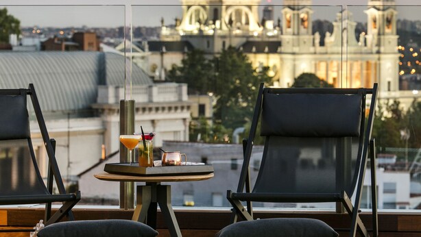 A rooftop terrace with two lounge chairs, a small table with drinks, and a view of a large cathedral with domes.
