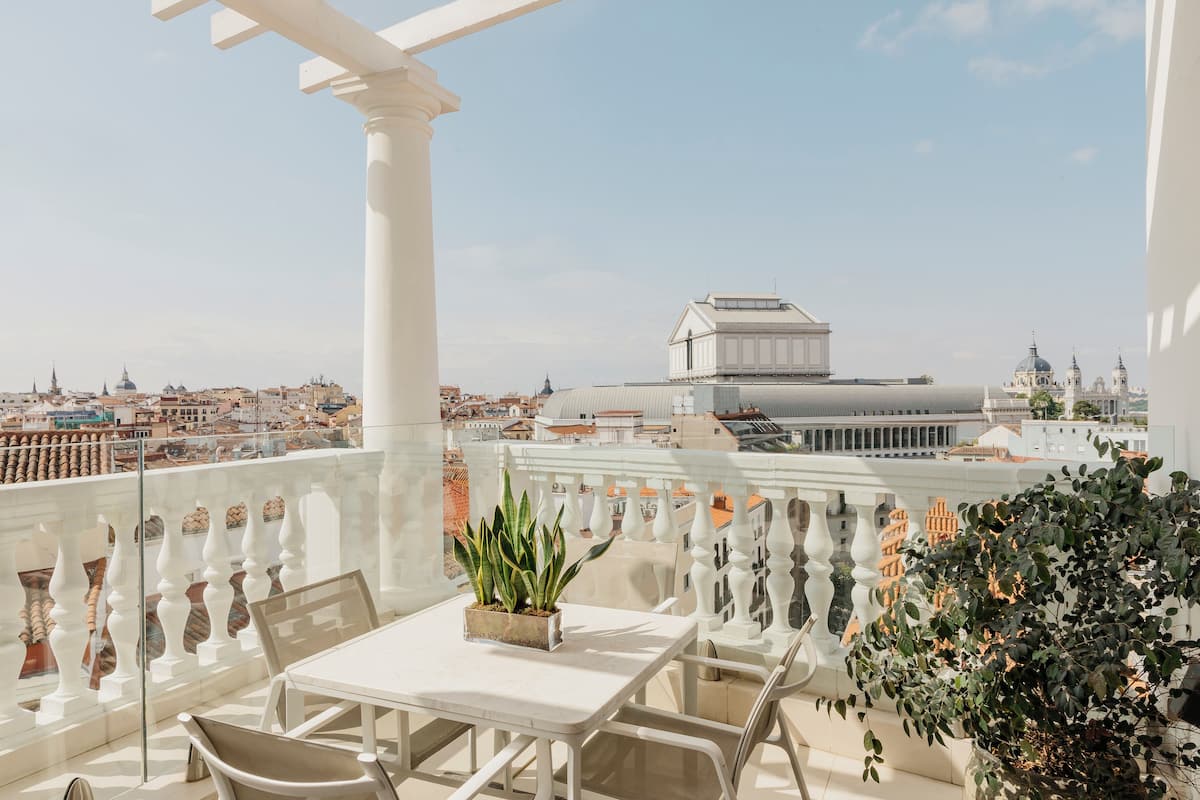 A balcony with a white railing, a table, and chairs. There is a potted plant on the table.
