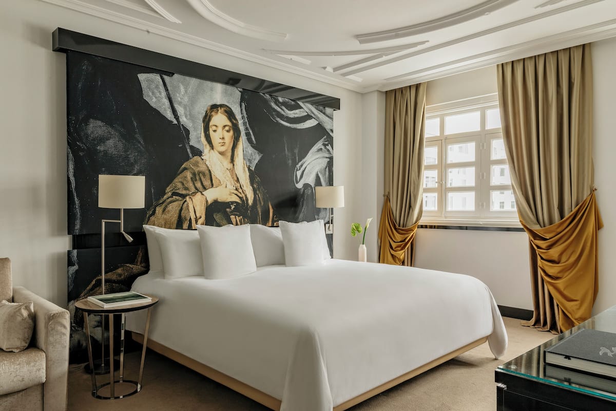 A spacious bedroom with a large bed, two bedside tables, a nightstand, and a large abstract painting on the wall.