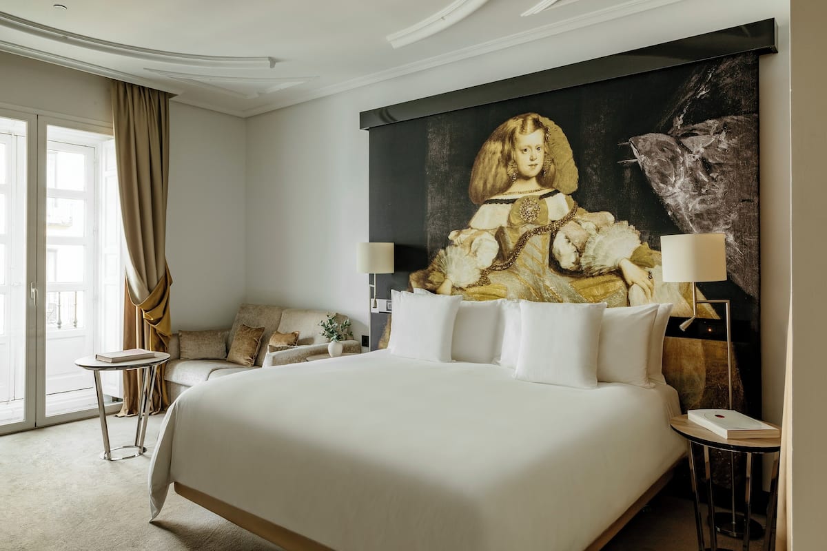 A hotel room with a large bed, a painting on the wall, a sofa, and a small table with a lamp.