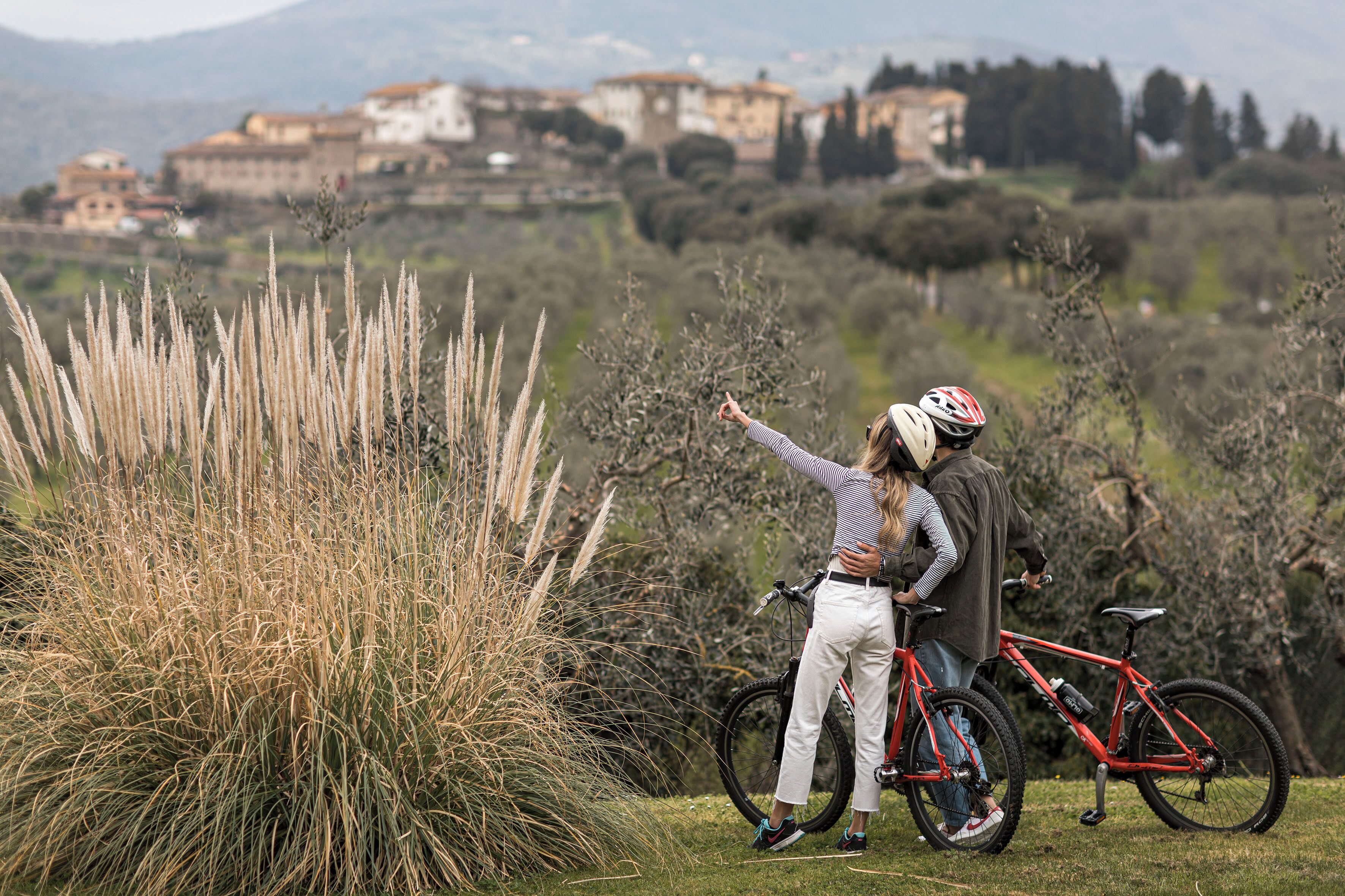 A person pointing at something in a grassy area with a red bicycle nearby.