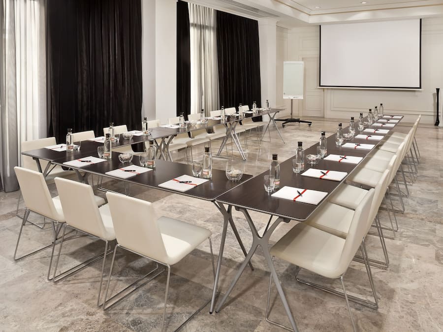 Un salón de conferencias con una larga mesa, sillas blancas y una pantalla para proyector.