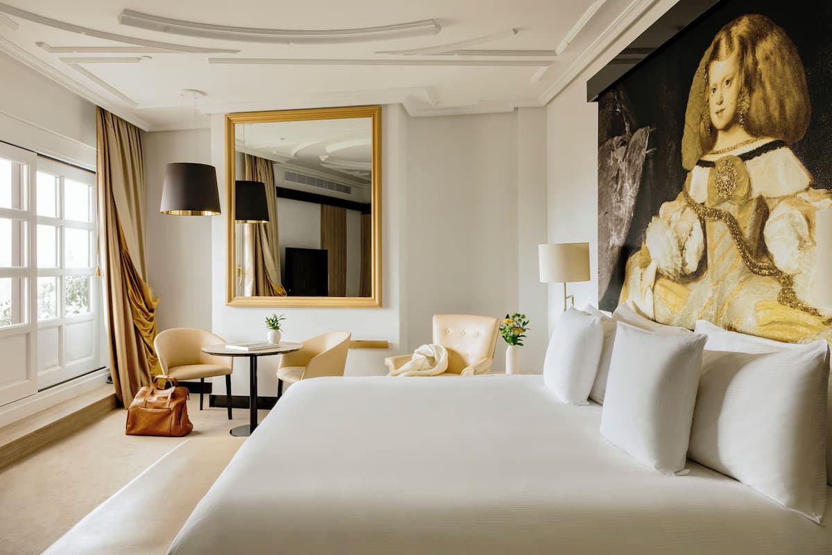 A hotel room with a large bed, a sitting area with a table and chairs, a large mirror, and a painting on the wall.