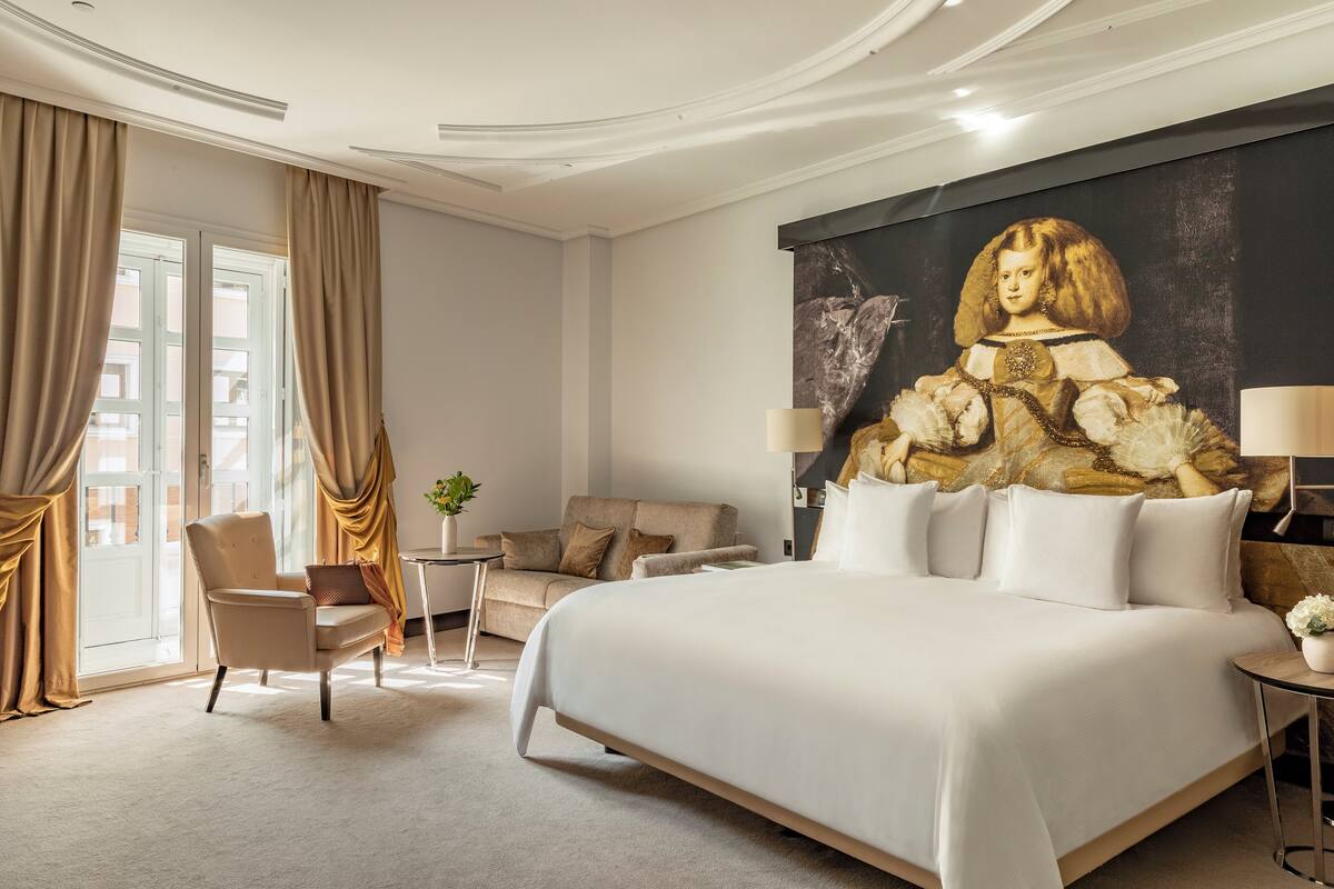 A modern hotel room with a large bed, a sofa, a chair, and a painting on the wall.
