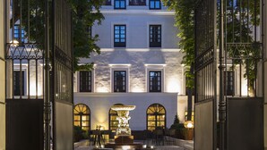 A courtyard with a fountain, a building with arched windows, and a wrought iron gate.