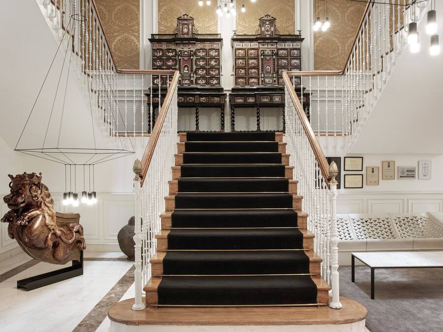 Una imponente escalera con peldaños alfombrados de color negro, barandillas blancas y un pasamanos de madera.
