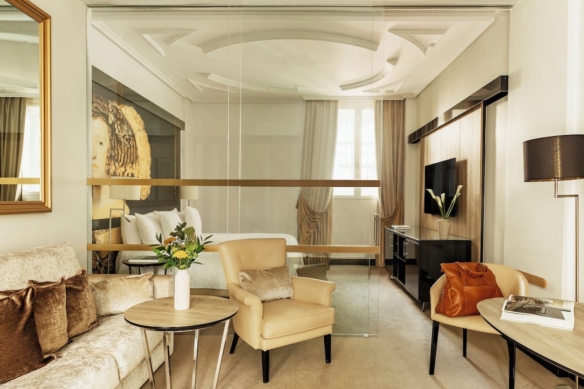 A modern hotel room with a sofa, armchair, and a small table with a vase of flowers.
