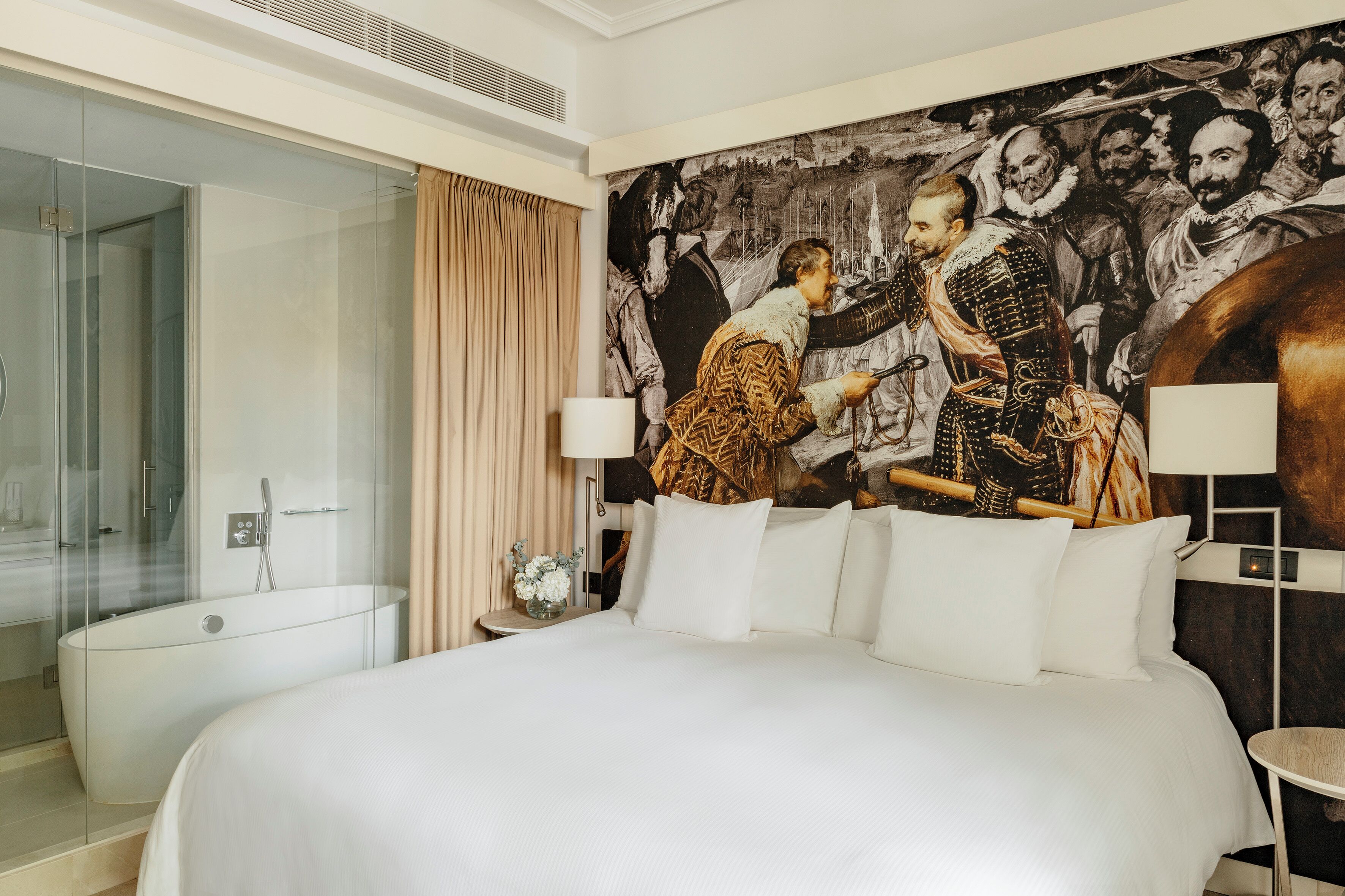 Habitación de hotel moderna con una cama grande, cabina de ducha con paredes de vidrio y un mural en la pared.