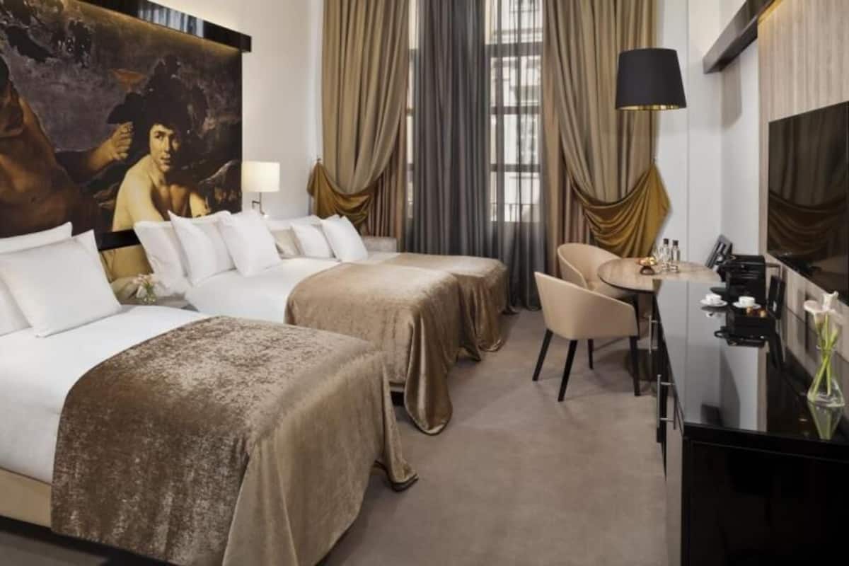 A hotel room with two beds, a desk, a chair, a large painting, and a TV.