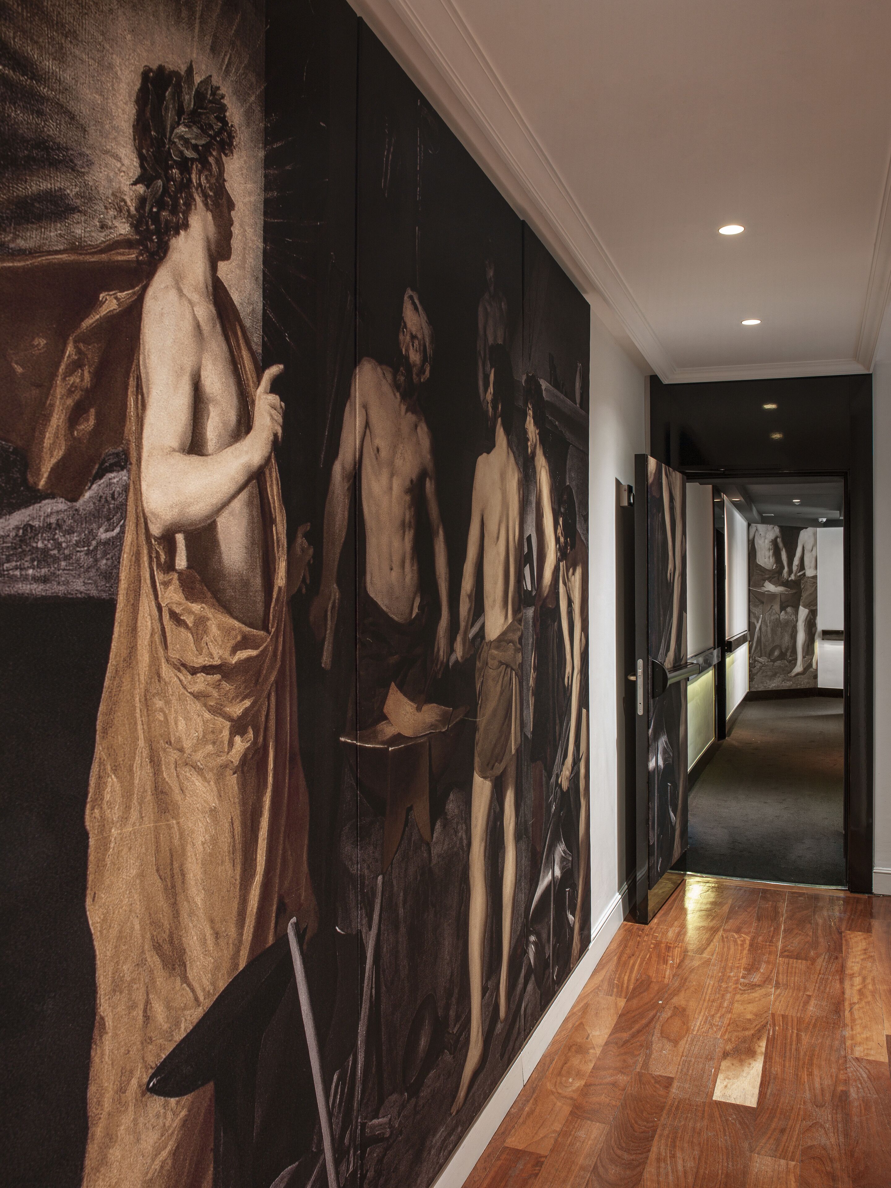 A hallway with a large mural of classical figures, wooden flooring, and a modern interior design.