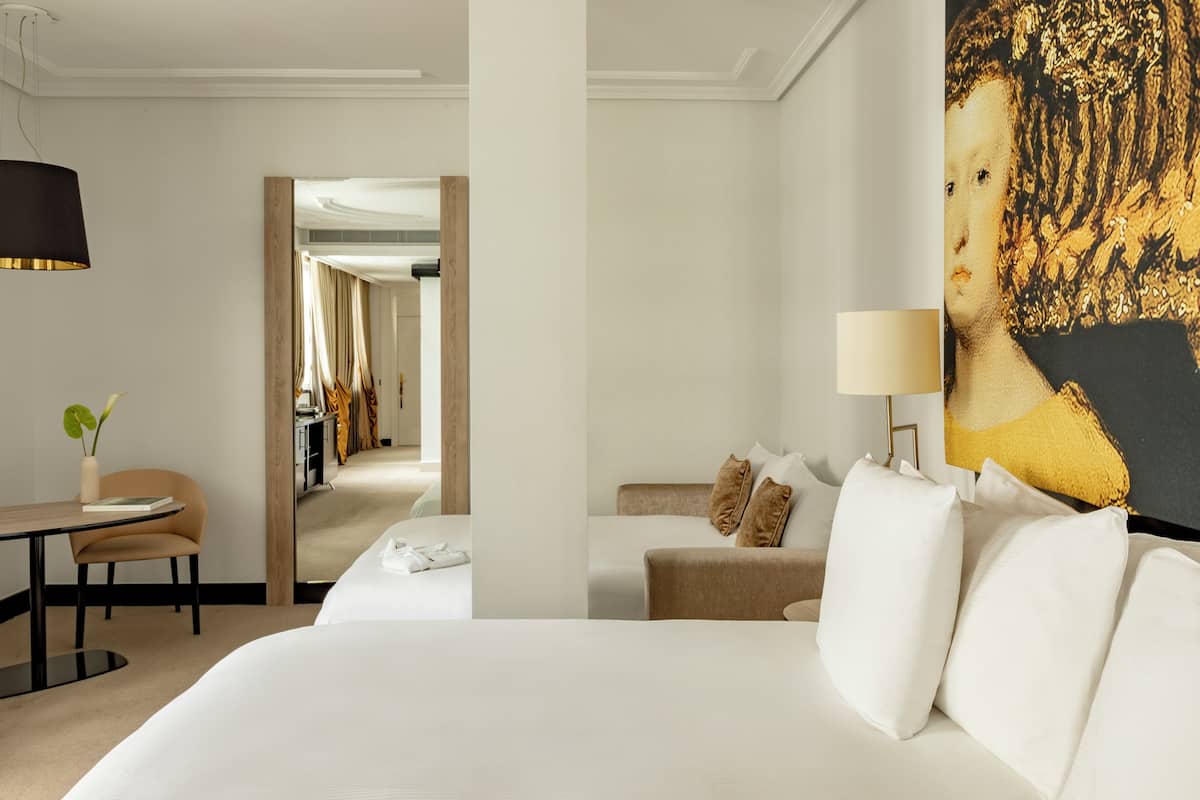 A hotel room with a large bed, a desk with a chair, a lamp, and a painting on the wall.