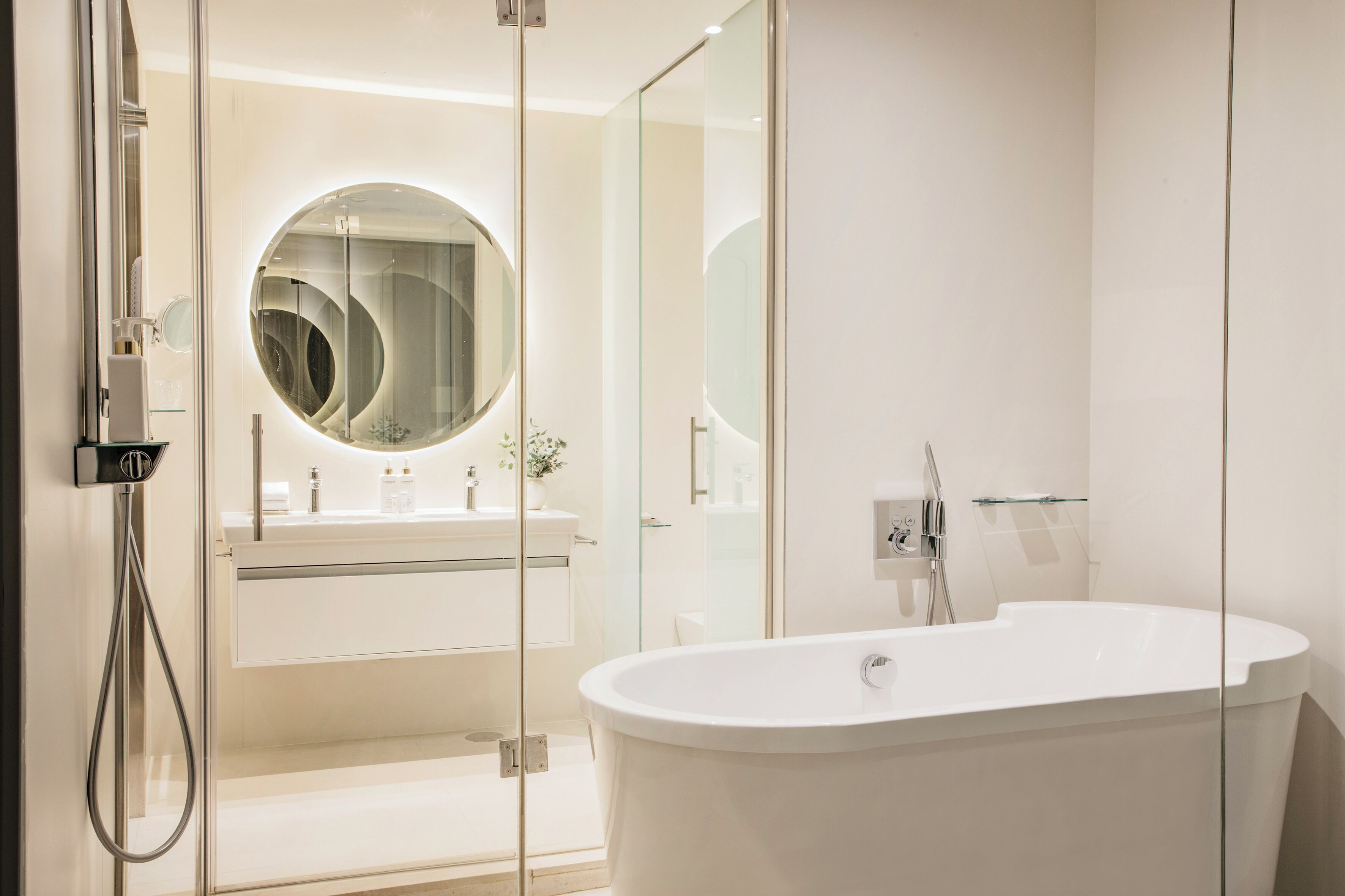A modern bathroom with a freestanding bathtub, a glass-enclosed shower, and a round mirror.