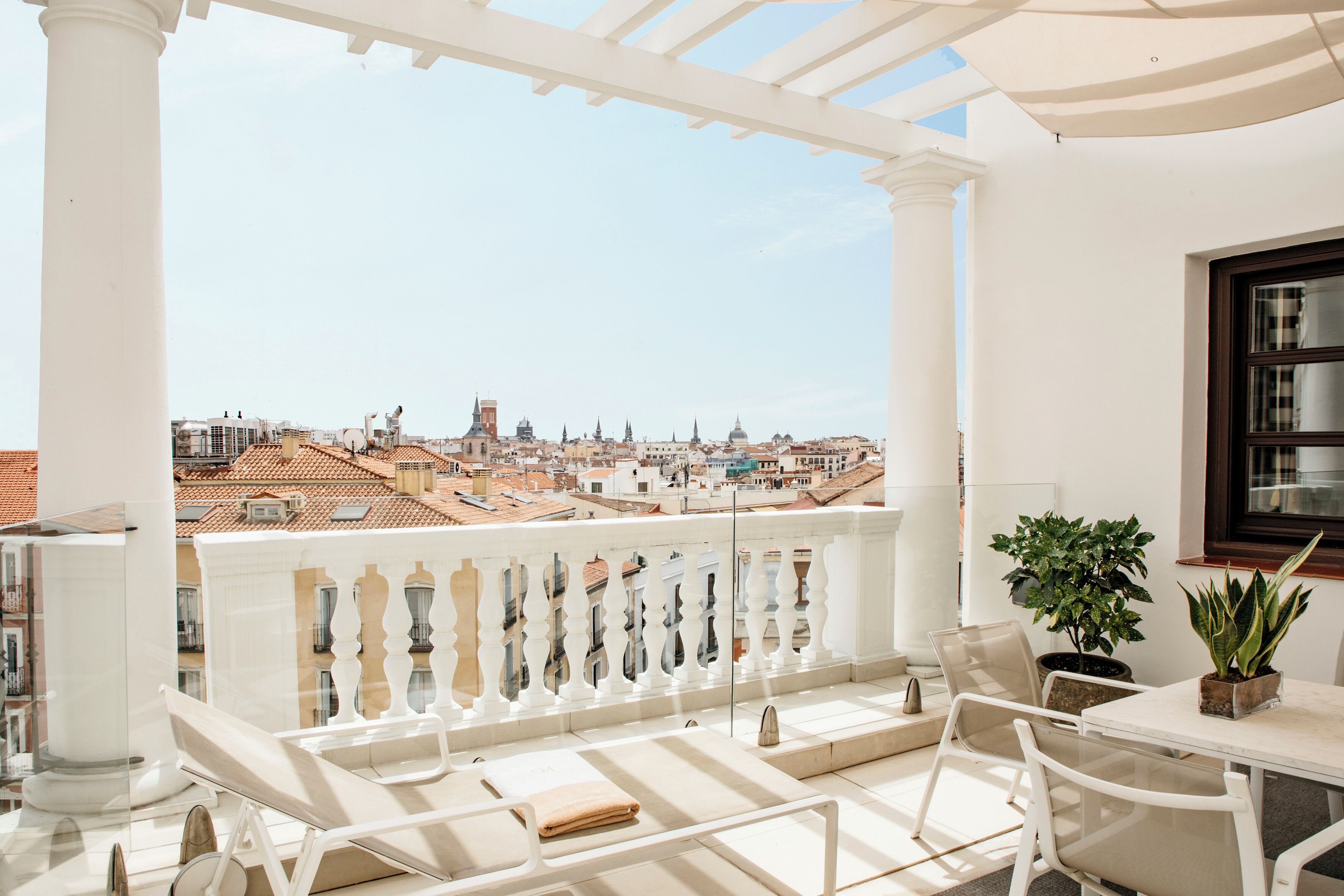 A balcony with a white railing, a table, chairs, and potted plants.