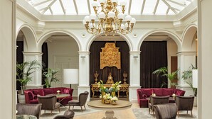 A luxurious lobby with a grand chandelier, red velvet sofas, and a central decorative piece.