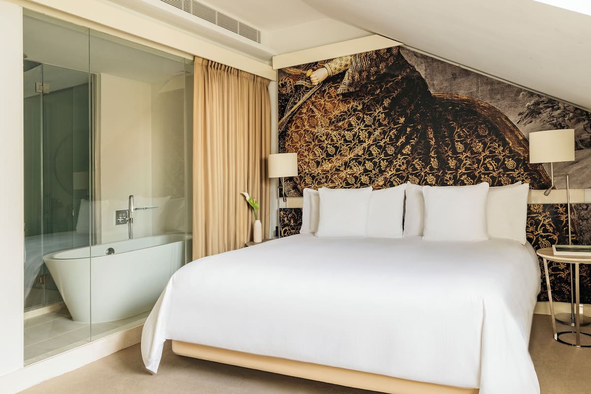 A hotel room with a large bed, a glass-enclosed shower, and a decorative wall mural.