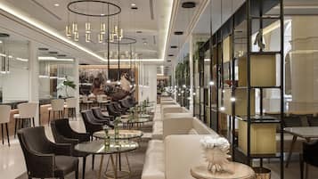 A modern hotel lobby with a long reception desk, seating areas, and a large mirror reflecting the space.